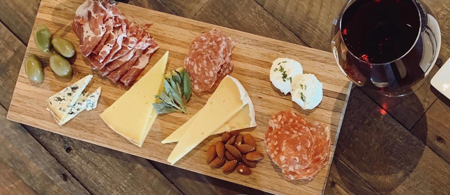 Wooden board with cheese and charcuterie. Glass of red wine on the side.