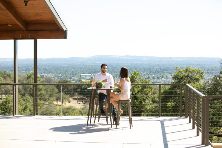 Two people sitting at a table drinking wine on the Veranda with west Sonoma County view behind them