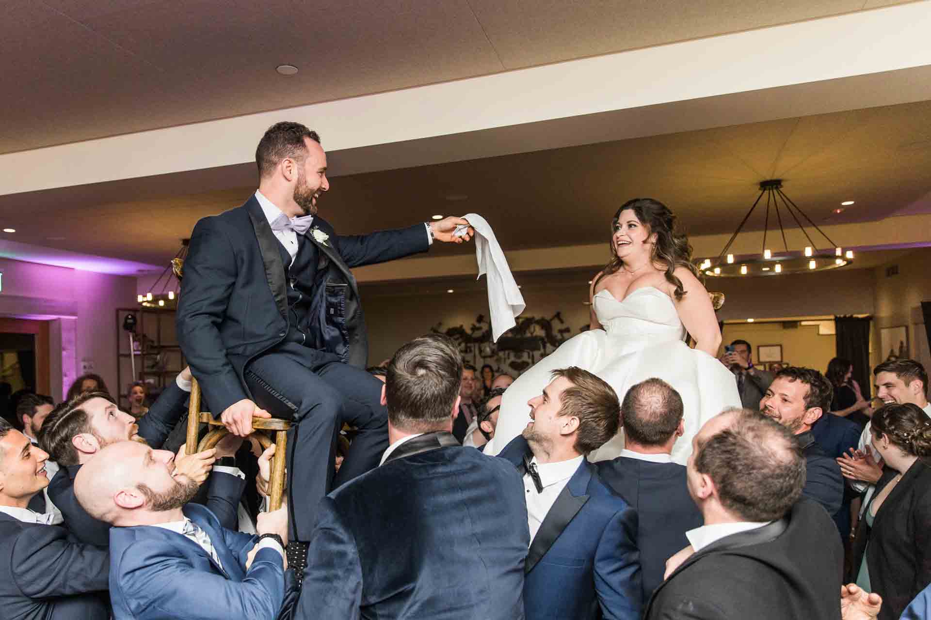 A newlywed couple shares in traditional chair dance on the indoor dance floor at Paradise Ridge Winery, illuminated by romantic lights and surrounded by friends.